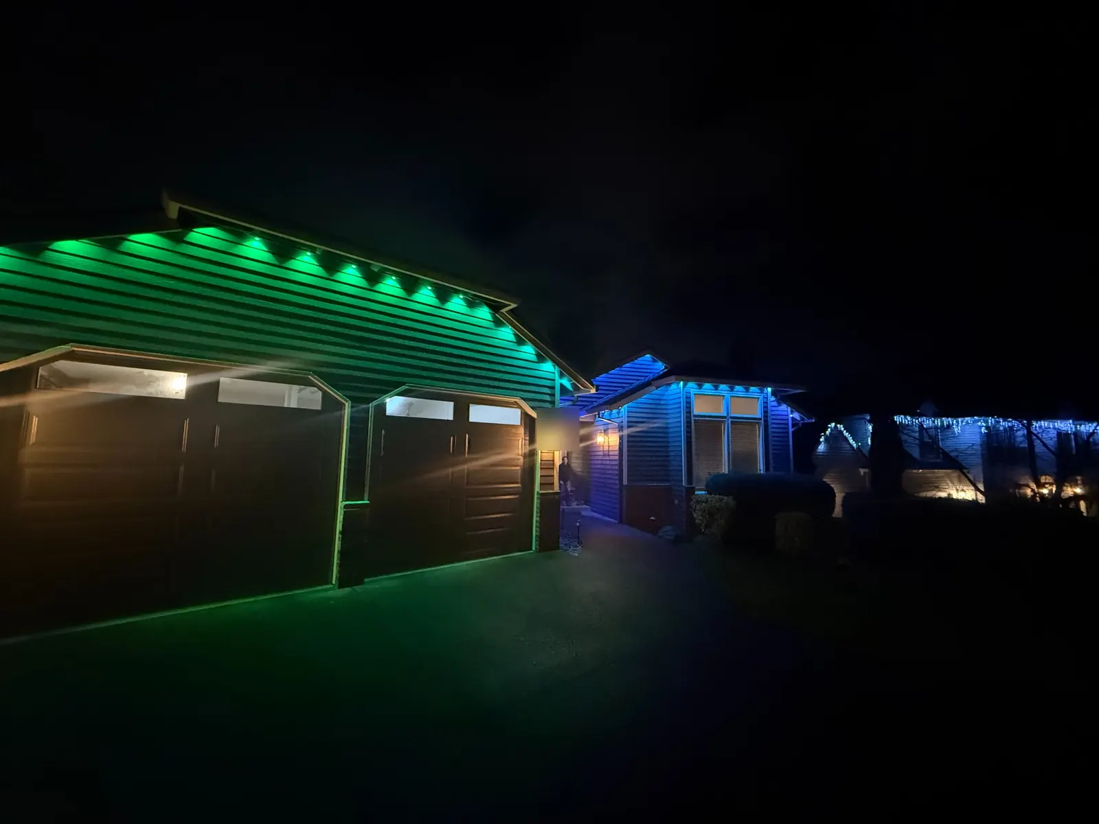 Permanent roofline LEDs set to green over the garage and blue over the entry wing of a home at night