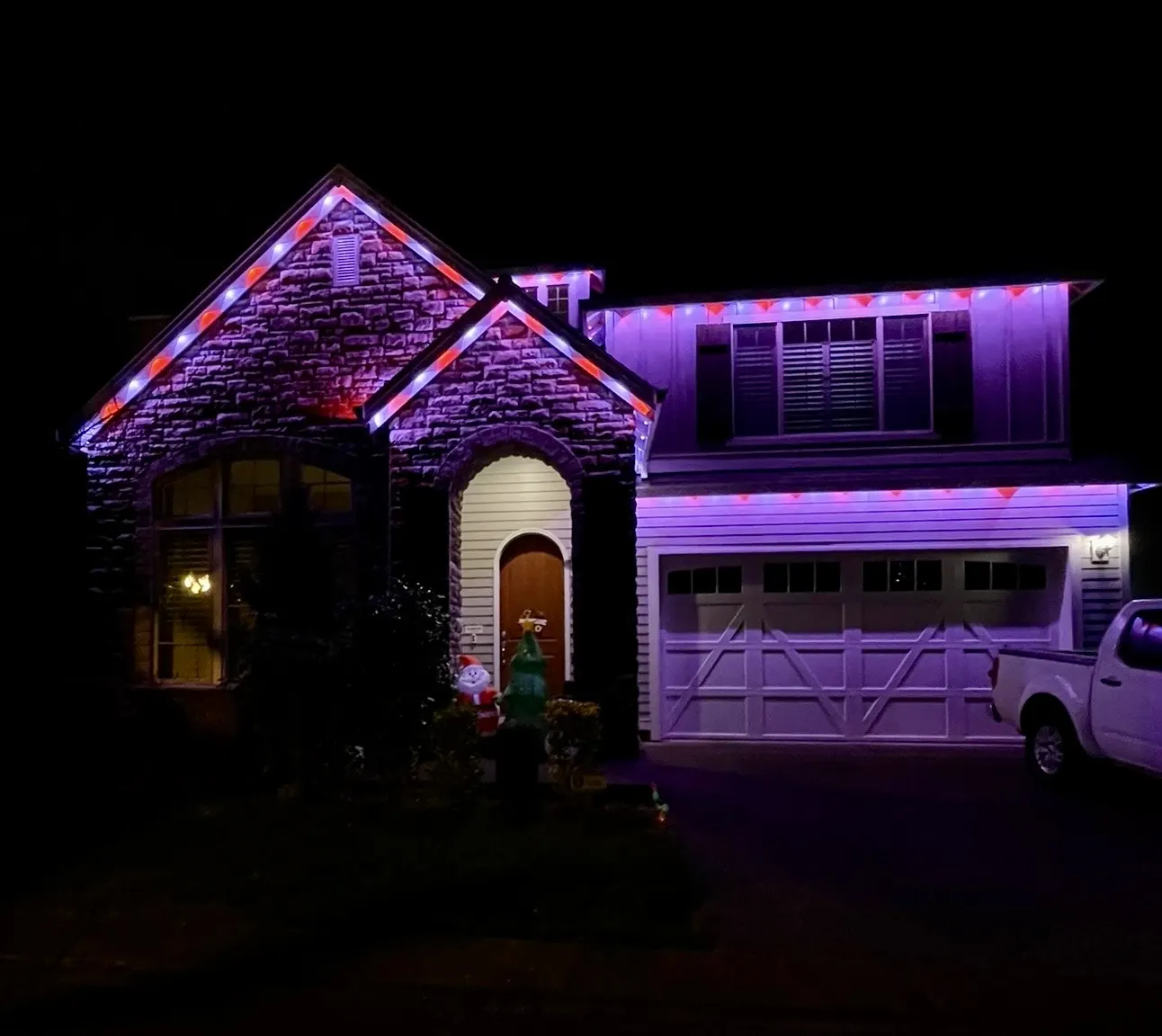 Stone-front home with permanent LEDs alternating red and white along the gables with a purple facade wash