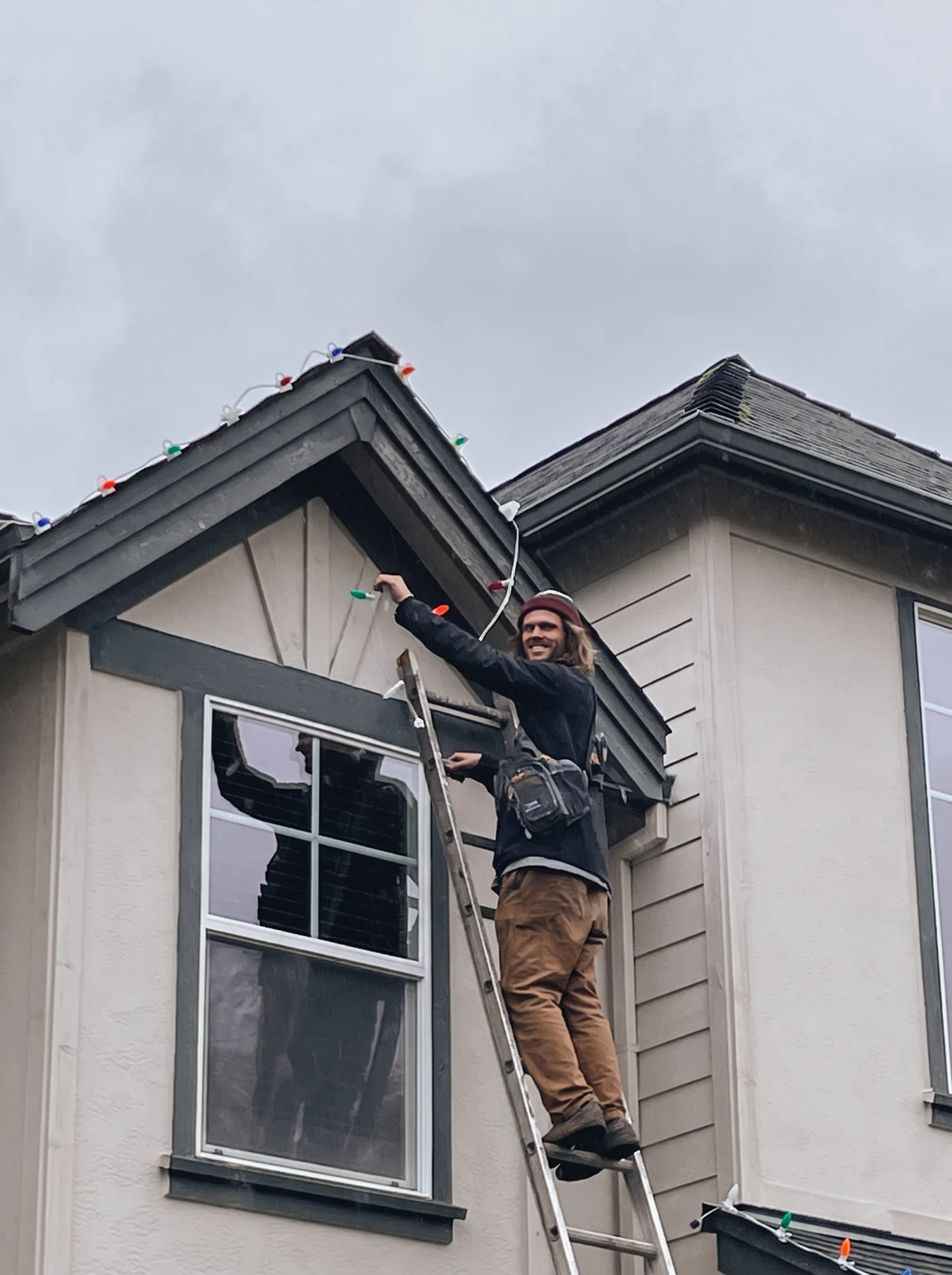 North Pole Lighting Co. founder Maarten installing multicolor Christmas lights along a Portland-area roofline