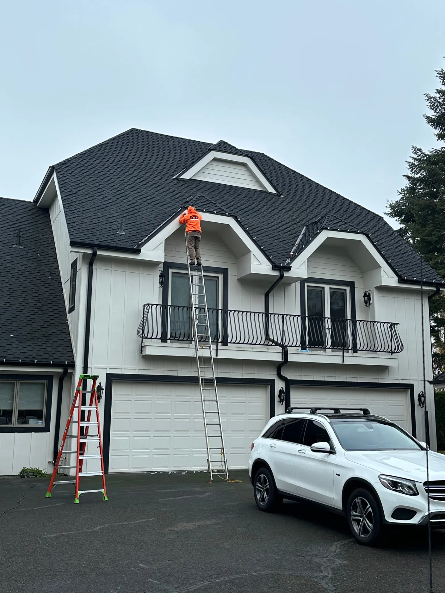 North Pole Lighting Co. installer on a ladder clipping C9 bulbs along the roofline of a two-story home during a daytime installation