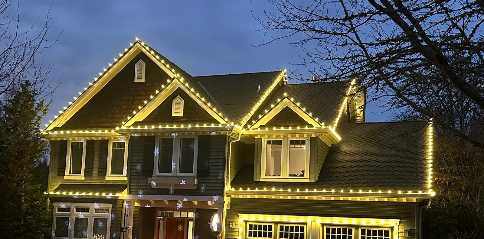 Craftsman-style home with warm white C9 lights traced along multiple gables and eaves at dusk