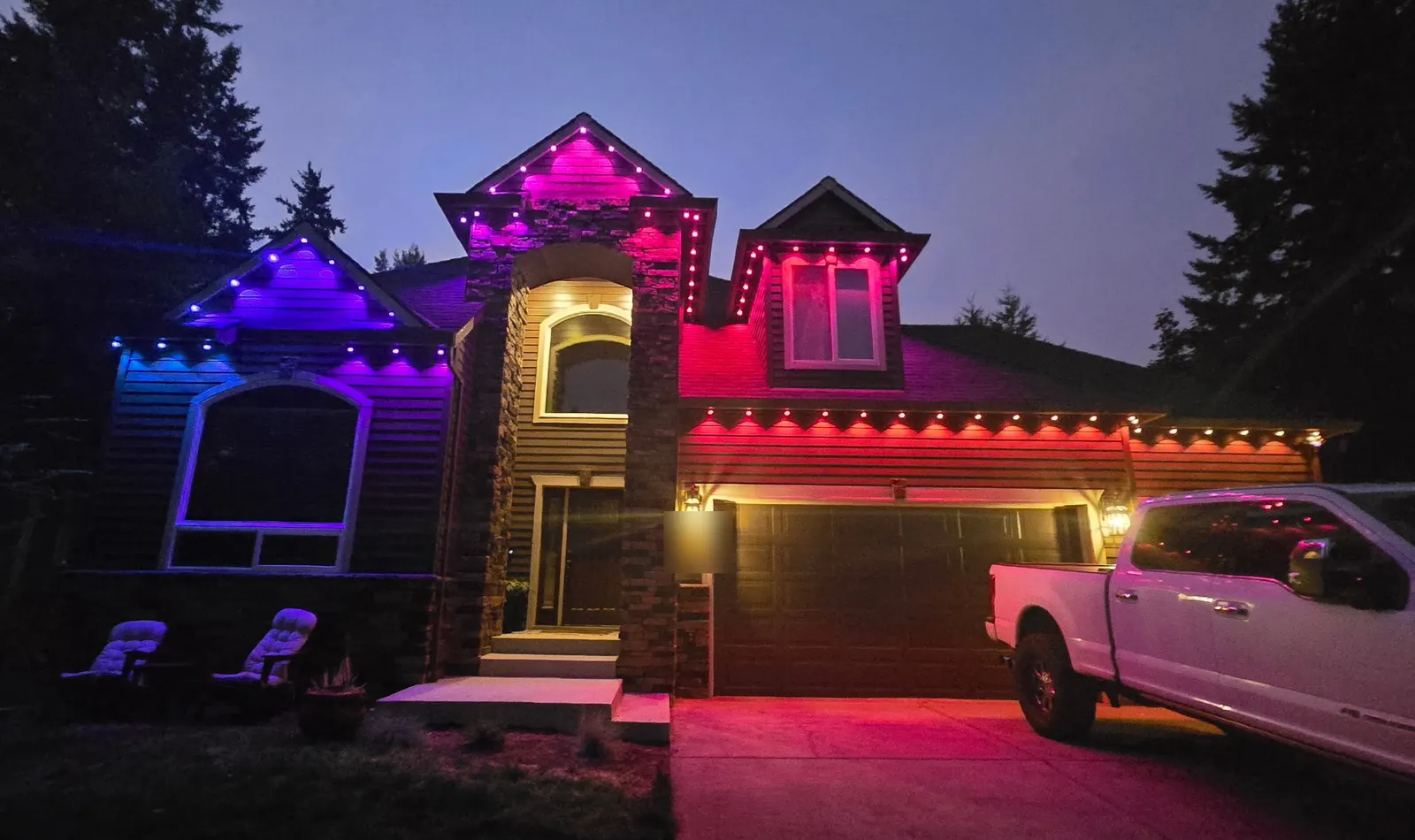 Two-story home with permanent architectural LEDs washing each gable in blue, magenta, and red at dusk